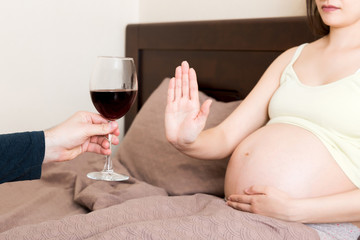 Close up of pregnant woman staying in bed refuses to drink wine and makes stop gesture to the glass. No alcohol during pregnancy concept