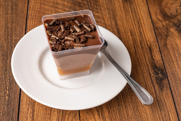 Fine chocolate dessert on a white plate with spoon on a wooden table surface.
