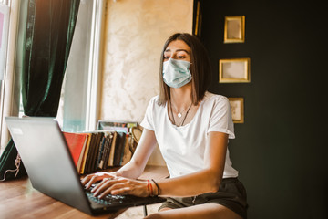 Casual woman freelancer in face mask using laptop for remotely working online in cafe