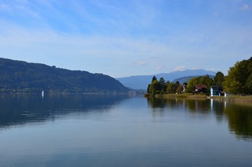 Fototapeta na wymiar Ossiacher Lake in Kaernten (Carinthia) in autumn, Austria, view from village of Bodensdorf, mountains on horizon, blue sky background