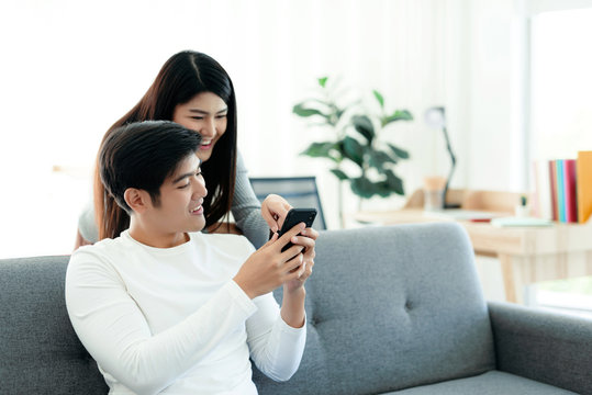 asian couple sits in the living room of their home on their mobile phones.