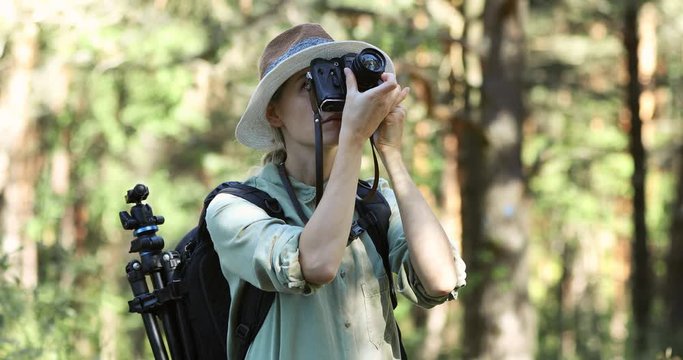 female photographer taking picture of nature with analog film camera in forest