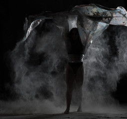 young athletic girl with long hair dances with a piece of cloth in a cloud of white flour