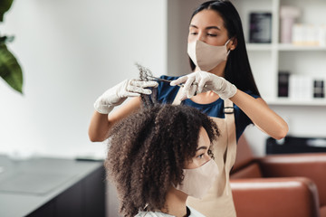 Black woman in protective mask visiting hairdresser at beauty salon