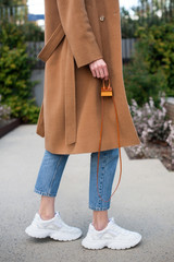 Fashionable young woman wearing beige wool coat. She is holding trendy mini bag in hands. Street style. 