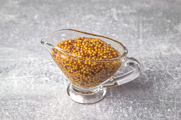 French mustard in a glass sauceboat on a grey background. Dijon mustard