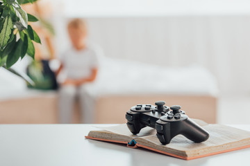 KYIV, UKRAINE - JULY 21, 2020: selective focus of joystick on open book, and silhouette of child sitting on bed near school backpack © LIGHTFIELD STUDIOS