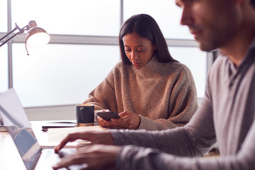 Businessman Working On Laptop At Desk Collaborating With Female Colleague Using Mobile Phone