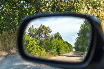 Rearview car driving mirror view green forest and village road.