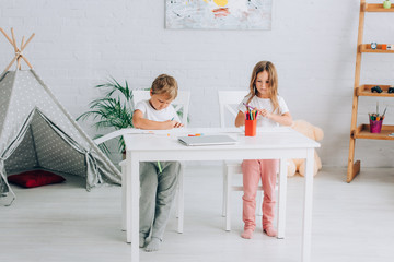 brother and sister in pajamas drawing with felt pens at table near kids wigwam © LIGHTFIELD STUDIOS
