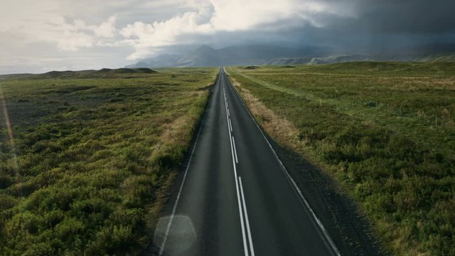 Aerial view of beautiful landscape with a highway in Iceland in summertime. Drone flying over asphalt road passes through the field.
