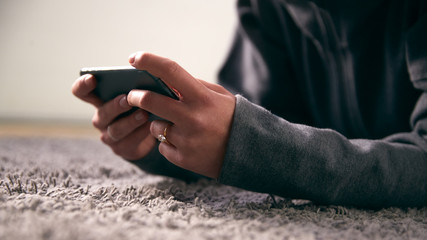 Close Up Of Woman At Home Looking At Social Media And Text Messages On Mobile Phone Lying On Carpet