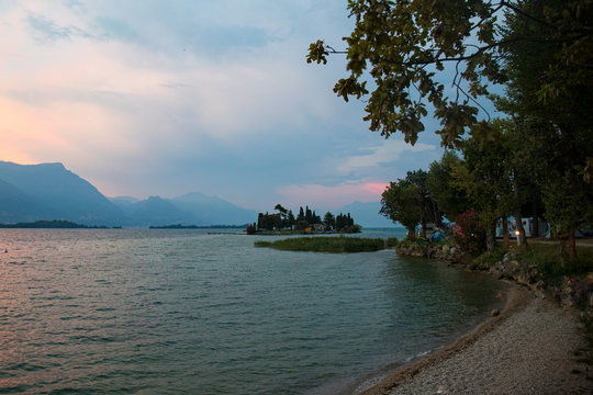 View of Garda Lake and San Biagio island at pink and blue misty sunset in Manerba del Garda, Italy.