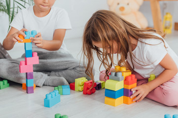 cropped view of boy playing with building blocks near sister while sitting on floor in pajamas