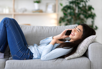 Obraz premium Positive Asian Girl Relaxing On Couch, Talking On Cellphone With Friends