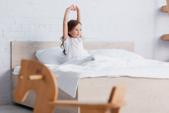 Selective Focus Of Awakened Kid Stretching While Sitting In Bed