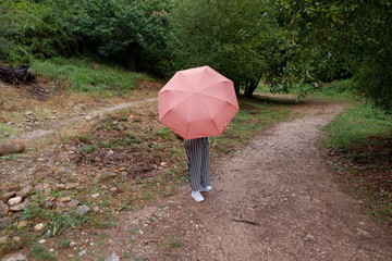 Mujer en el campo con pantalones a rallas y paragüas rosa