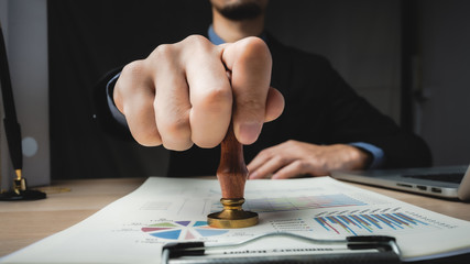 Close-up Of A Person's Hand Stamping With Approved Stamp On Document At Desk.