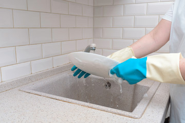 female hands in blue gloves wash a plate in a white kitchen