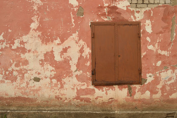 Vintage background with the texture of an old plastered damaged brick wall with a window closed by metal shutters.