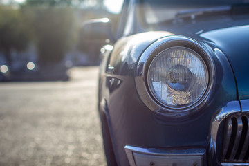 Close-up of a round headlight on an old car. On against the sun