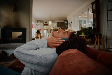 Happy african young woman sitting on sofa with headphones listening to music at home