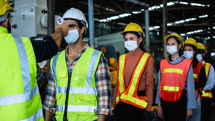 Industrial worker and engineer stand in line to check flu with infrared thermometer before enter to work and protect Coronavirus or Covid-19, safety and protection as working in manufacturing