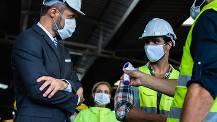 Industrial worker and engineer stand in line to check flu with infrared thermometer and manager...