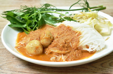 rice noodles dressing with meat ball fish coconut milk curry sauce and fresh vegetable on plate