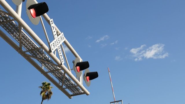 Level crossing warning signal in USA. Crossbuck notice and red traffic light on rail road intersection in California. Railway transportation safety symbol. Caution sign about hazard and train track.