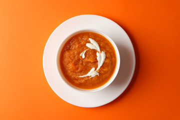 Bowl of pumpkin puree on orange background, top view