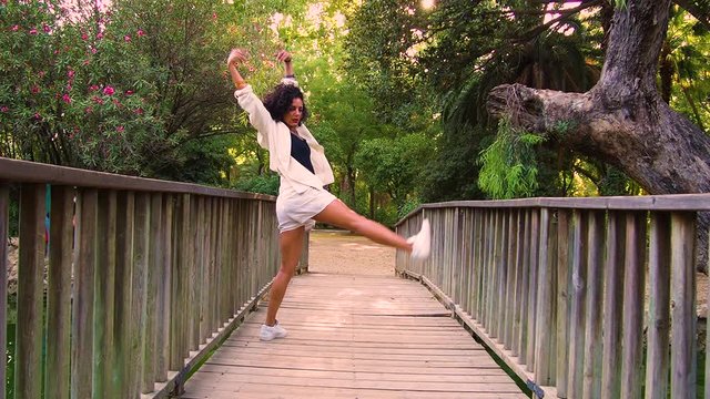 Mujer joven vestida de blanco bailando en un puente de madera y un bosque en el fondo