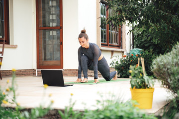 Fit young woman learning stretching exercise while watching video on laptop in backyard