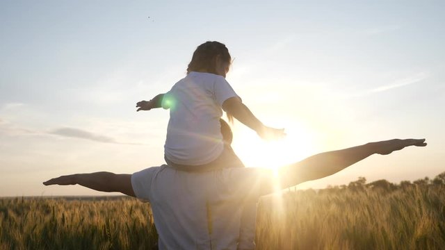 dream future concept. kid girl daughter sits on father neck play airplane in superhero aviator pilot depict the plane with his hands. silhouette at sunset. happy family people in the park. parent dad