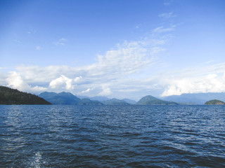 Beautiful landscape with sea, mountains and white clouds on blue sky near Vancouver.