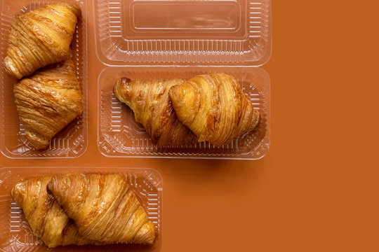 Freshly Baked Croissants In Plastic Packaging On An Orange Background. Takeaway Food Concept. French And American Croissants Are Enjoyed Worldwide.Croissants Background: Top View, Flat Lay