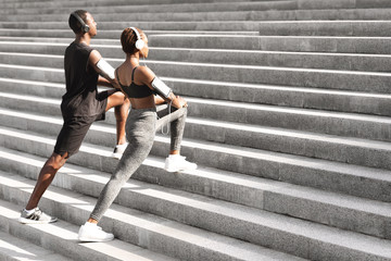 Motivated Black Couple Warming Up Muscles Before Jogging Outdoors On Urban Stairs