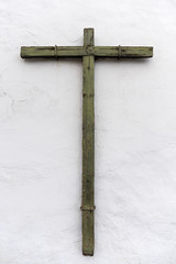 Altes verwittertes Kreuz aus Holz an einer weißen Wand, befestigt mit Bügeln aus Metall