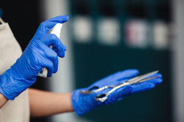 Master in medical gloves spraying disinfectant on scissors, close up