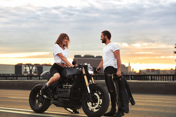 Romantic date on motorbike. Young woman sits on a motorcycle and looks at the man who comes to her. Couple in love with sunset on the bridge in the city