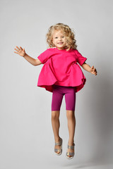 Blonde kid girl with curly hair in stylish casual shorts and t-shirt has fun jumping