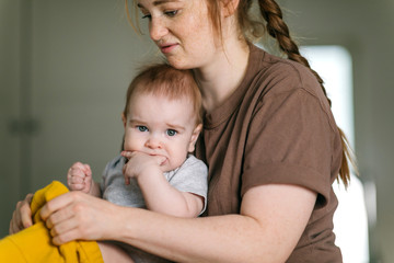 Young mother with a nine-month-old baby in the bedroom, thoughtful and tired