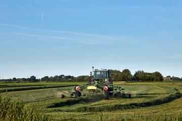 Bauer auf seinem Traktor beim Heu wenden, an einem sonnigen Tag