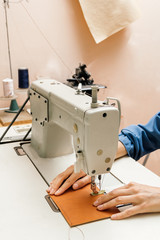 Side view of professional sewing machine in the workshop, woman's hands hold a piece of yellow leather