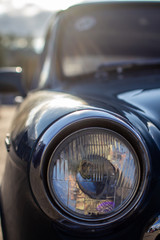 Close-up of a round headlight on an old car. On against the sun