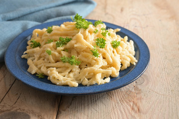 Homemade spaetzle served with parsley garnish on a blue plate and a rustic wooden table, traditional egg pasta in Schwaben, southern Germany and Austria