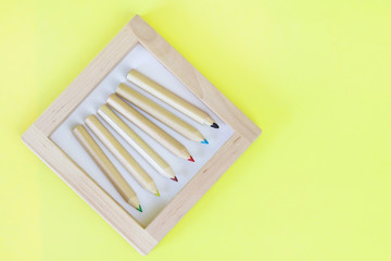 Colored pencils in a wooden frame on a yellow background. Copy space - concept of education, child development, back to school, creativity.