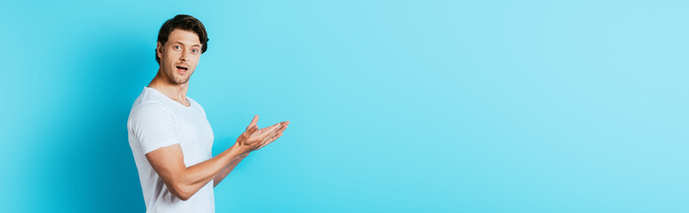 Panoramic shot of excited young man pointing with hands on blue background