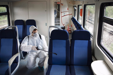 Public transportation healthcare. Man in white protection suit disinfecting and sanitizing subway...