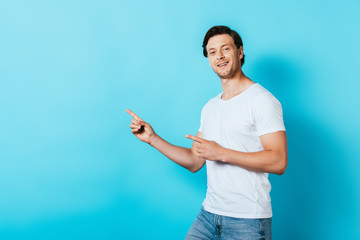 Man in white t-shirt pointing with fingers and looking at camera on blue background